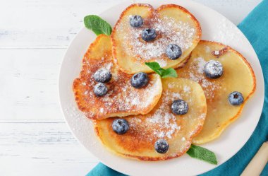 Yaban mersinli krep, pudra şekeri ve nane şekeri tabakta, beyaz arka plan manzaralı mavi peçete.