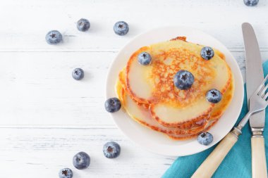 Yaban mersinli gözlemeler açık ahşap bir masada, bıçak, mavi peçete, çatal, üst manzara