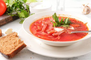 Ekşi kremalı borş ve maydanozlu beyaz tabak, kaşık, ekmek beyaz ahşap masada, kırmızı çorba, 