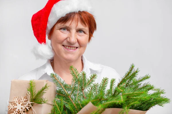 Old woman in santa\'s hat with present and tree branches close up with white background