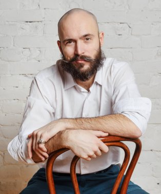 Portre, sakallı ve bıyıklı genç kel adam. Beyaz gömlekli. Odada bir sandalyede oturuyor., 