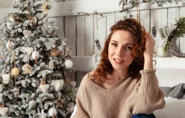 Kafkasyalı esmer güzel kız. Arka planda Noel ağacı var. Açık bej süveter.
