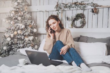 Kafkasyalı güzel kız yatağında oturuyor ve elinde bir fincan kahveyle dizüstü bilgisayarına bakıyor.