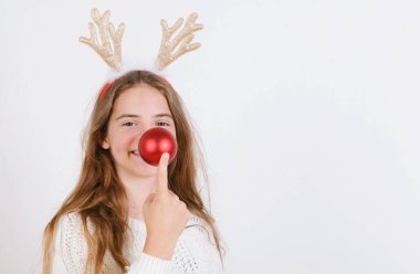 Beyaz kazaklı ve boynuzlu genç kız burnuna kırmızı bacağa dokunuyor Noel gülümsemesi gibi basit arka plan minimalist tatiller.