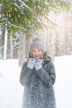 Beyaz şapkalı, eldivenli ve siyah ceketli genç bir kadın kışın karların altındaki ormanda bir ladin ağacının dallarının altında duruyor.