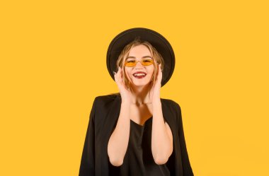 Siyah ceketli, şapkalı, güneş gözlüklü, sarı yüzlü bir kadın. 