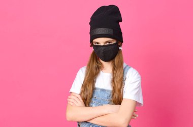 Pembe arka planda kızgın bir ifadeyle siyah maskeli ve şapkalı bir genç kız.