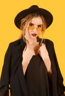 Siyah ceketli, güneş gözlüklü ve sarı şapkalı bir kadın. 