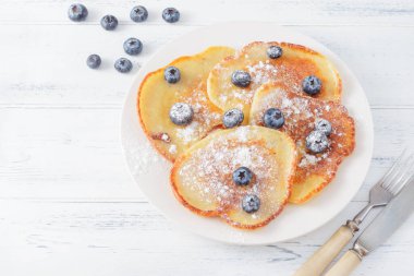 Böğürtlenli krep ve pudra şekeri tabakta, çatalda, bıçakta beyaz ahşap arka planda, üst manzarada