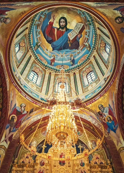 The altar with painted ceiling of Curchi Monastery, in Orhei, Moldova. Golden chandelier with glowing lights suspended from cupola. Different saints icons, traditional for Christian Orthodox churches