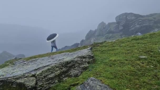 一个带着雨伞的孤独男子站在布满薄雾的岩石山岗上的后视镜 一个孤独陌生的人在雨中的忧郁和情绪化的场景 — 图库视频影像