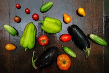 fresh vegetables scattered on a dark wooden background, peppers, eggplants, tomatoes and cucumbers scattered on a dark background