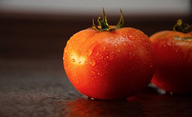 Koyu ahşap arkaplanda su damlaları olan domatesler.