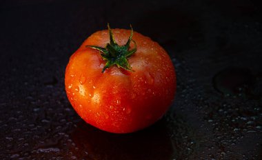 Koyu arkaplanda olgun domates. Yakın plan su damlalarıyla kaplı domates..