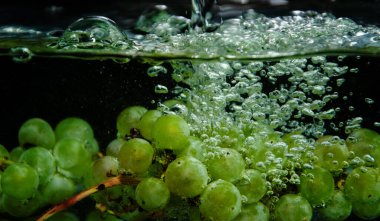 Yeşil üzümler arka planda berrak sulara sıçrıyor. Su sıçramaları ve kabarcıkları olan yeşil üzümler.