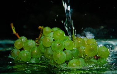 Yeşil üzümler arka planda berrak sulara sıçrıyor. Su sıçramaları ve kabarcıkları olan yeşil üzümler.