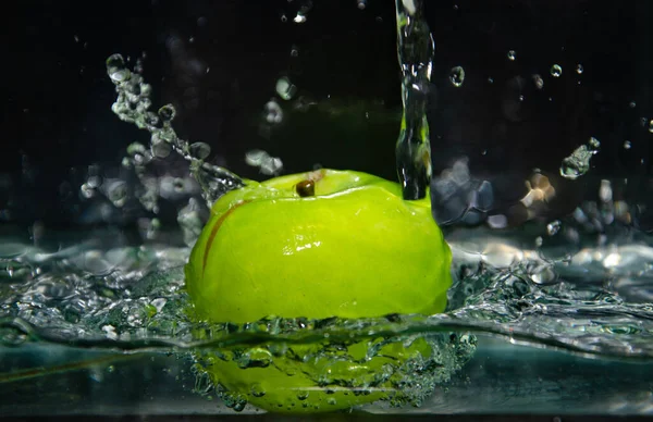 green apple thrown into water with splashes and bubbles. green apple in water