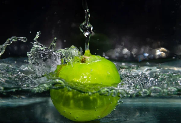 green apple thrown into water with splashes and bubbles. green apple in water