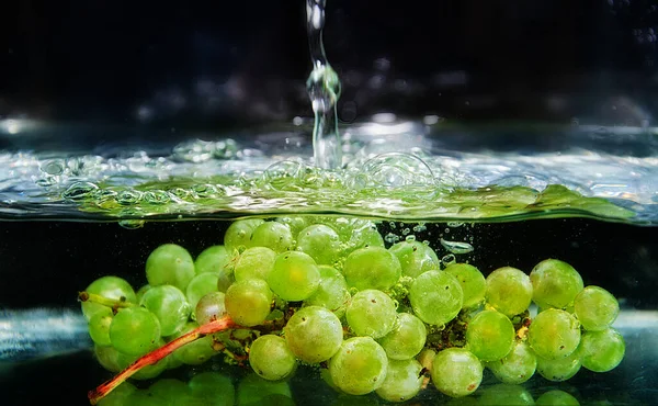 Bunches of green grapes splash into clear water on a dark background.green grapes with water splashes and bubbles