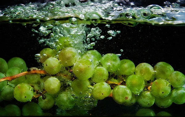 Bunches of green grapes splash into clear water on a dark background.green grapes with water splashes and bubbles
