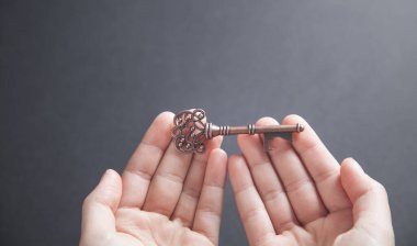 Siyah arkaplanda eski anahtarı tutan eller.