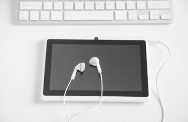 Kulaklıklı tablet ve beyaz masada bilgisayar klavyesi..