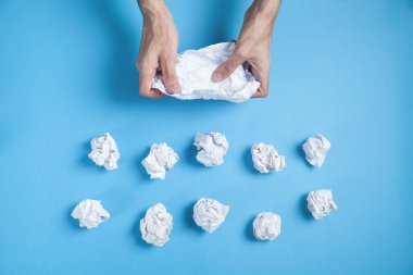 Mavi arka planda buruşmuş kağıt tutan erkek eller.