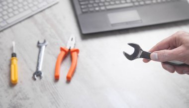 Erkek eli ingiliz anahtarı gösteriyor. Bilgisayar klavyeleri masanın üstünde. Bilgi İşlem. Destekle