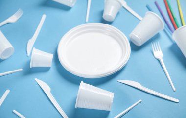 Mavi arka planda beyaz plastik tabak, bardak, çatal ve bıçaklar..