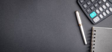 Siyah arkaplanda kalem, not defteri ve hesap makinesi.