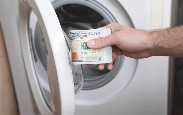 Male hand holding dollar in washing machine. Money laundering