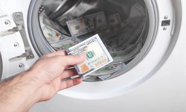 Male hand holding dollar in washing machine. Money laundering