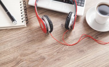 Kırmızı kulaklıklar, kahve, bilgisayar klavyesi, tahta masaya kalem ve not defteri..