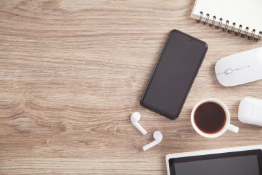 Kahve, akıllı telefon, kablosuz kulaklık ve ahşap masadaki diğer nesneler..
