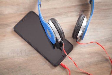 Mavi kulaklıklar ve ahşap masada akıllı telefon..