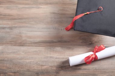 Tahta arka planda mezuniyet şapkası ve diploması var..