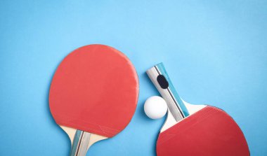 Masa tenisi raketleri ve mavi arka planda beyaz plastik bir top..