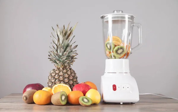 White blender with fresh fruits on the table.