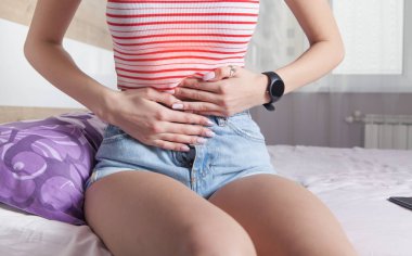 Bir kadın yatakta otururken midesi ağrıyor..