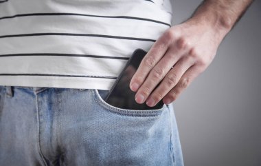Kot pantolonun cebine akıllı telefon koyan adam.