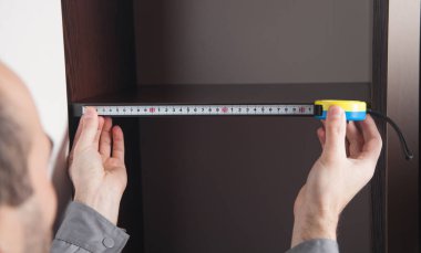 Eve yeni mobilya yerleştirilirken mezura kullanan adam.