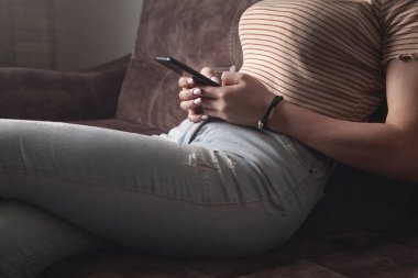 Kadın evdeki koltukta otururken cep telefonu kullanıyor..