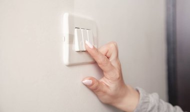 Duvardaki elektrik düğmesini çeviren kadın el..