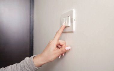 Duvardaki elektrik düğmesini çeviren kadın el..