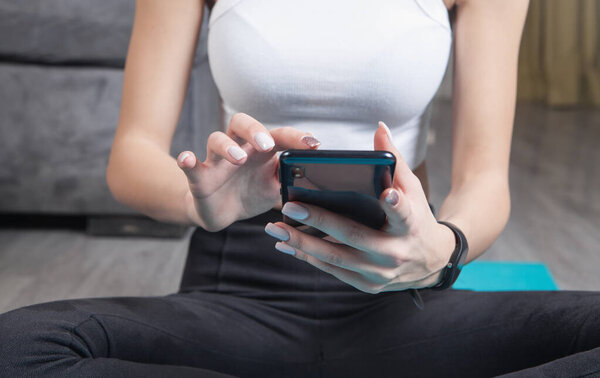 Young woman sitting on mat holding smartphone. Watching online workout