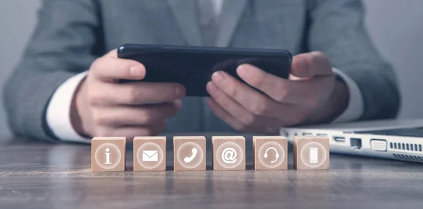 Man using smartphone. Contact symbols on wooden cubes