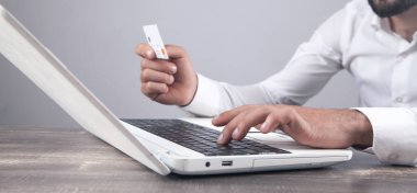 Dizüstü bilgisayar kullanan ve kredi kartı tutan bir iş adamı..