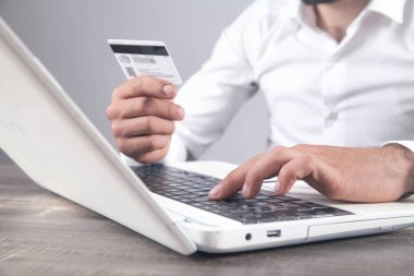 Dizüstü bilgisayar kullanan ve kredi kartı tutan bir iş adamı..