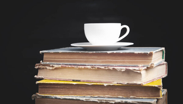 Stack book and cup of coffee on the black background.