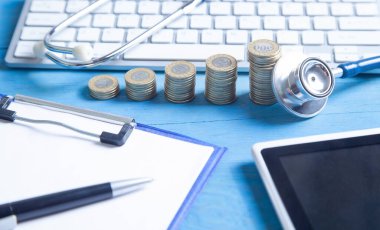 Mavi arkaplanda stetoskop, tablet, bilgisayar klavyesi ve bozuk paralar var..